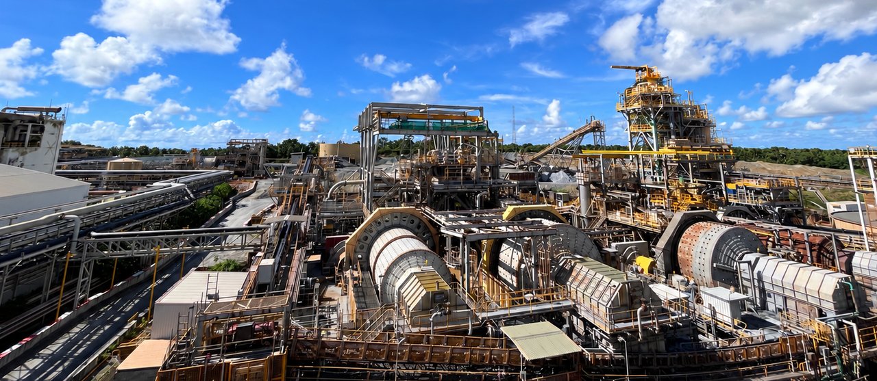A mineral processing plant seen from above — grinding mills, conveyors and walkways under an open sky.